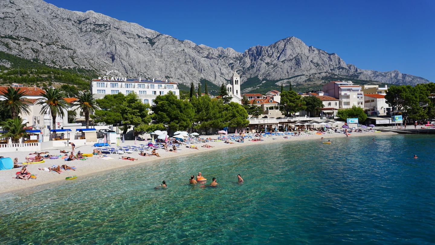 Kiesstrand und Uferpromenade von Baška Voda, dahinter das Biokovo-Massiv über dem Ort