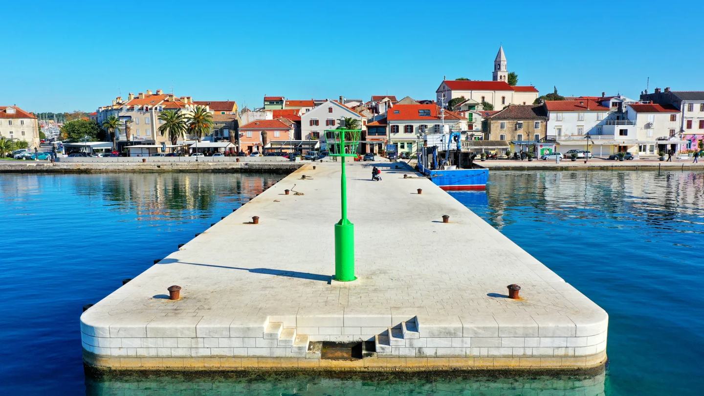 Die Hafenmole von Biograd na Moru mit grünem Leuchtfeuer, dahinter Uferpromenade und Glockenturm