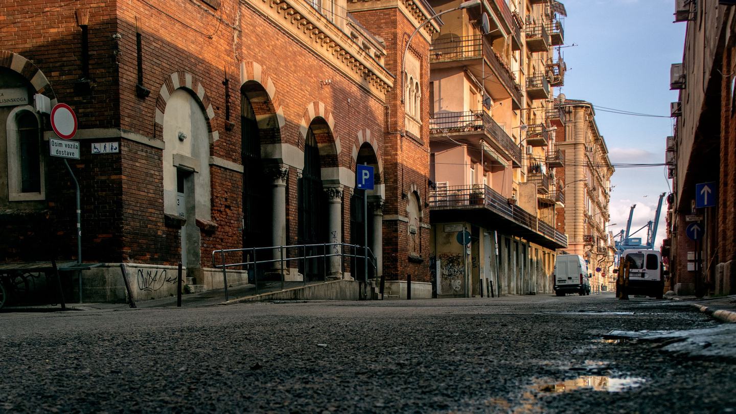 Eine Straße im Hafenviertel von Rijeka, Backsteinlagerhäuser mit den Hafenkränen am Ende