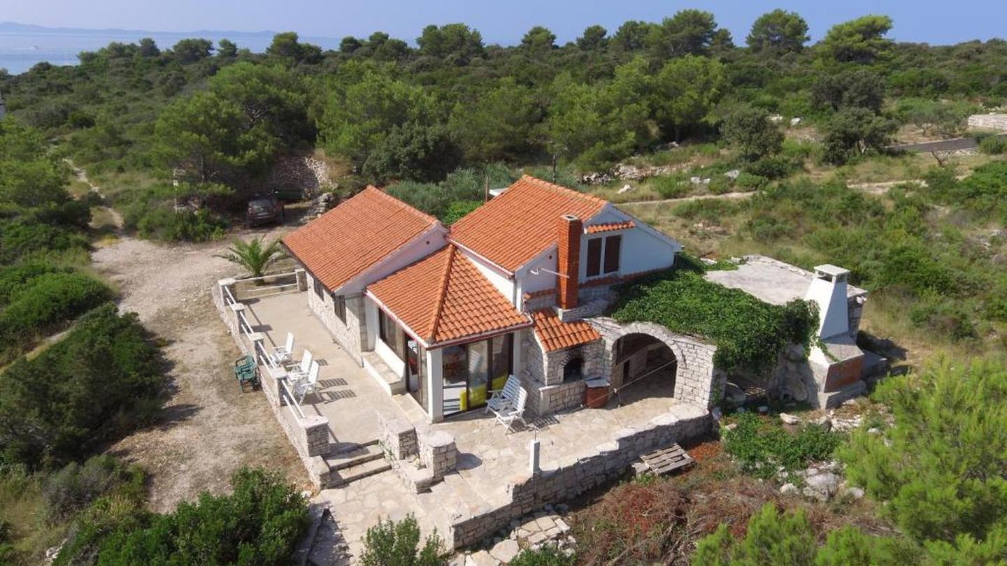 Ein steinernes Ferienhaus auf Šolta mit Terrasse und Außenkamin, umgeben von Pinien