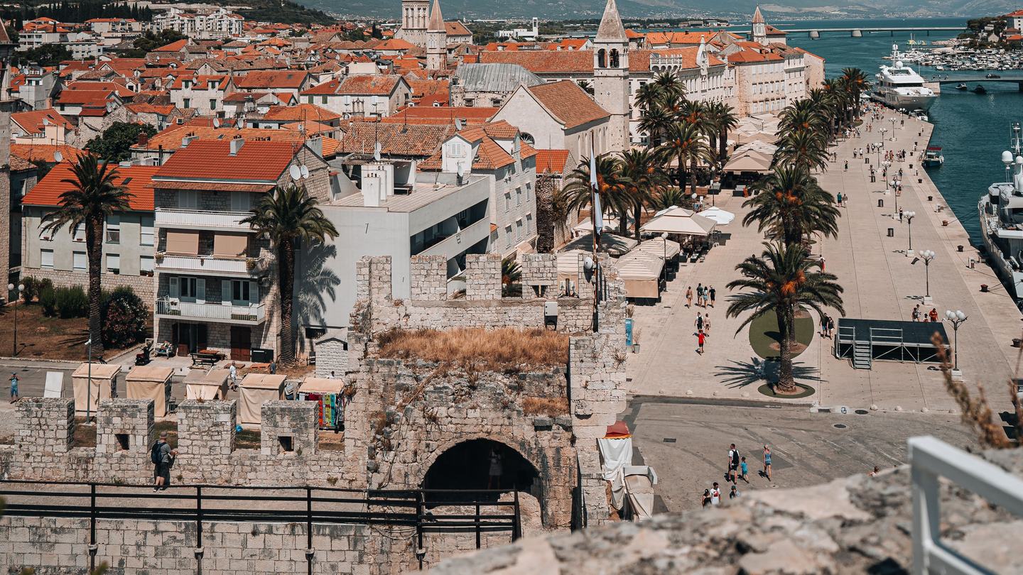Die Altstadt von Trogir von der Festungsmauer, die Riva mit Palmen und dahinter die Marina