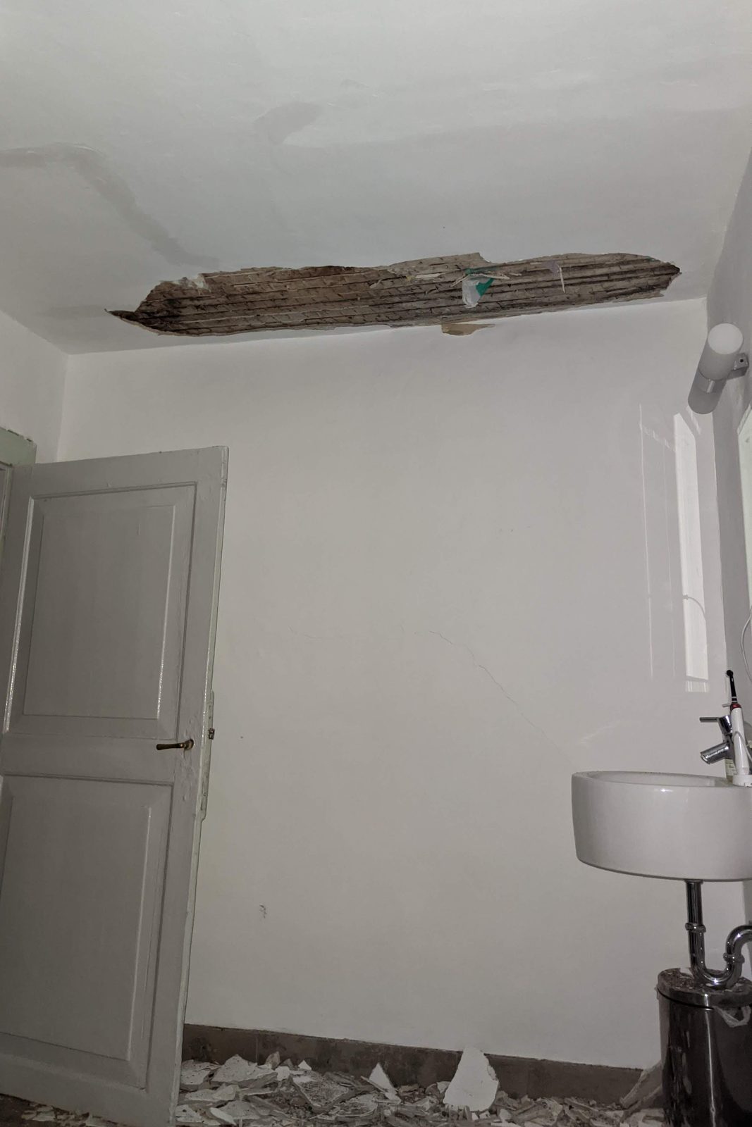 Badezimmer mit einem langen fehlenden Streifen Deckenputz, darunter auf Holz genagelte Schilfrohrmatten, Putzbrocken über den ganzen Boden verteilt