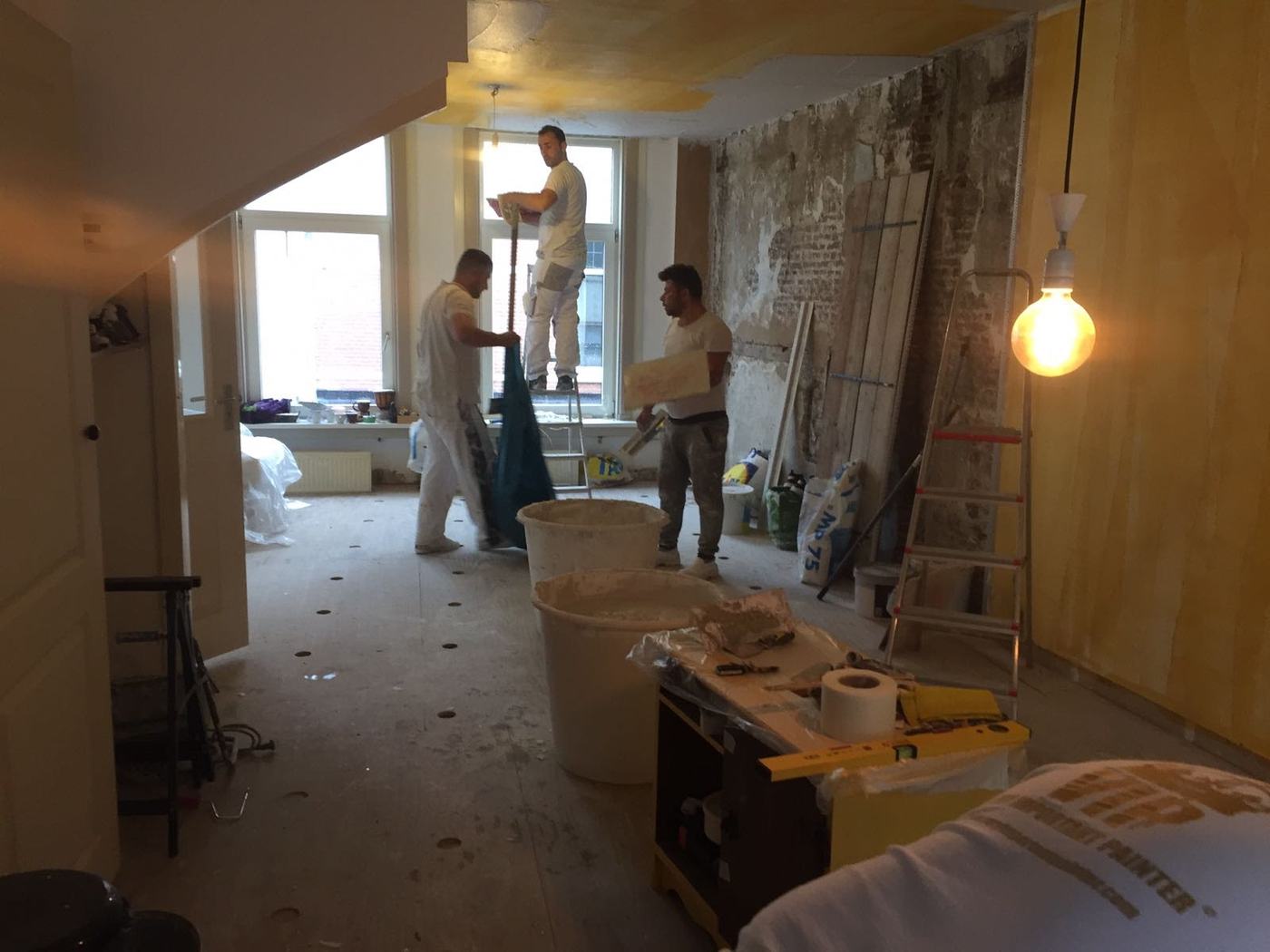 Drei Verputzer bei der Arbeit in einem bis auf den Ziegel entkernten Raum, Maschinenputz in Eimern, die Wand halb fertig